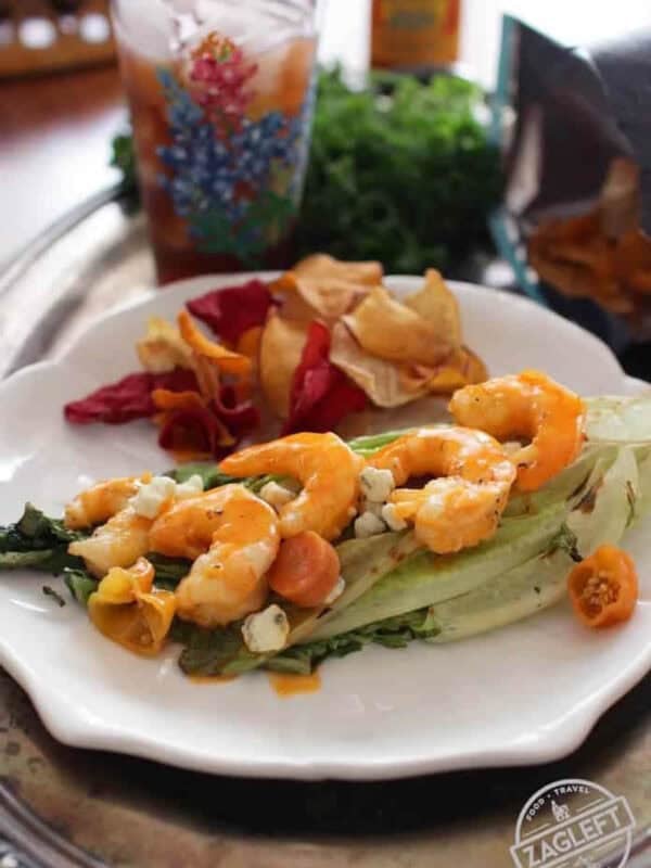 Grilled Buffalo Shrimp on grilled Romaine lettuce topped with blue cheese crumbles plated with chips