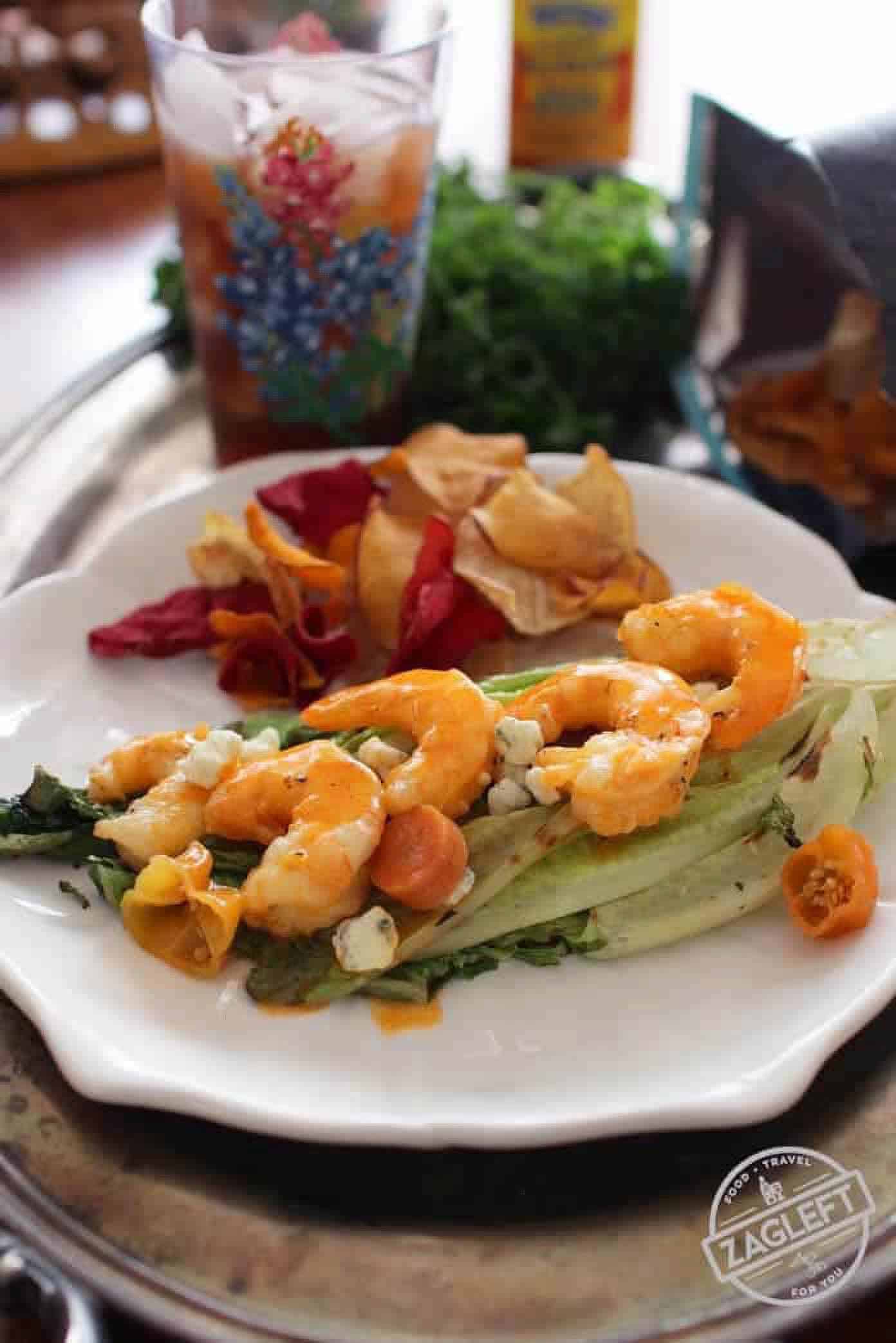 Grilled Buffalo Shrimp on grilled Romaine lettuce topped with blue cheese crumbles plated with chips