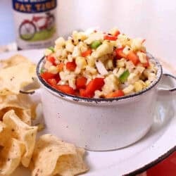 A bowl of corn salsa plated with tortilla chips next to a bottle of beer
