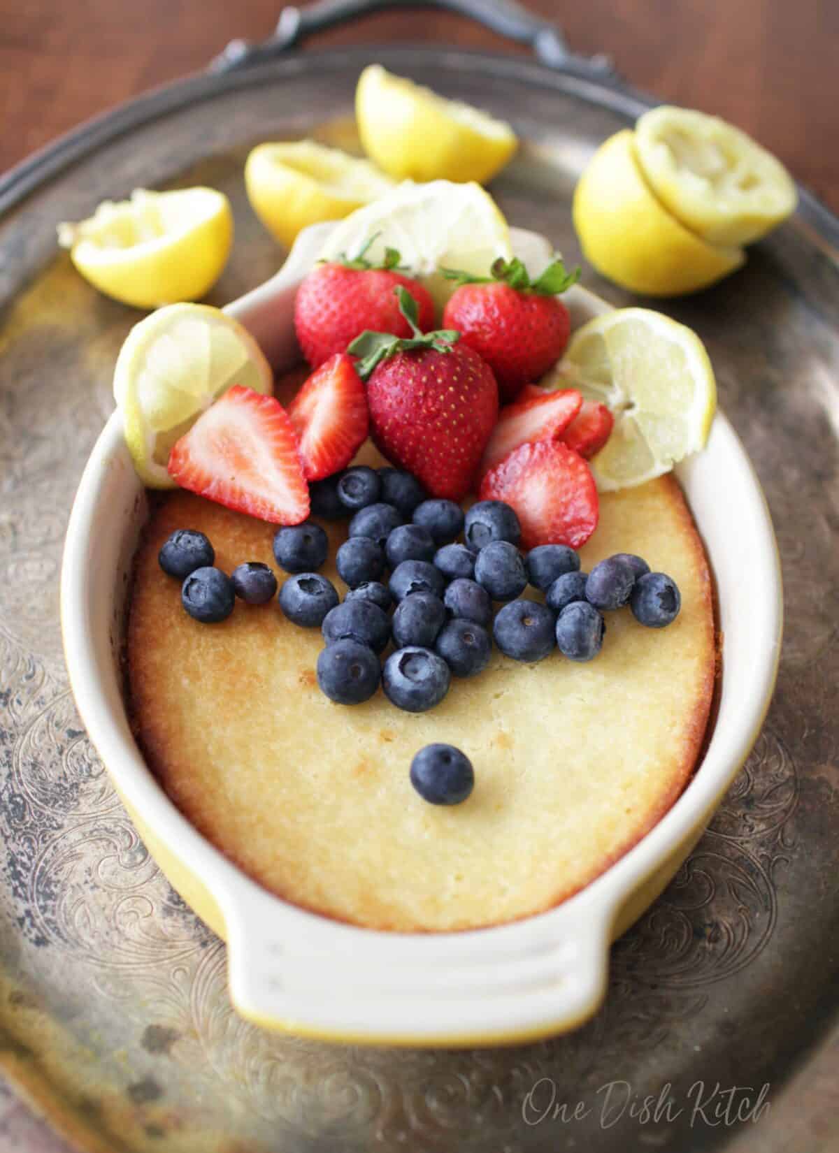 a cake baked in a yellow oval baking dish topped with blueberries, strawberries and slices of lemons.