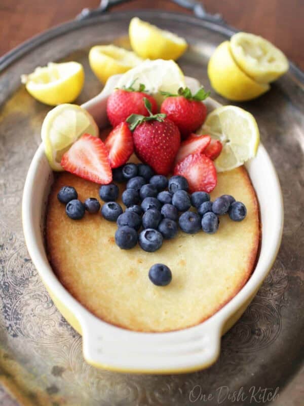 a cake baked in a yellow oval baking dish topped with blueberries, strawberries and slices of lemons.