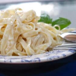 A plate of pasta with Alfredo sauce with a fork and spoon resting on the side of the plate.