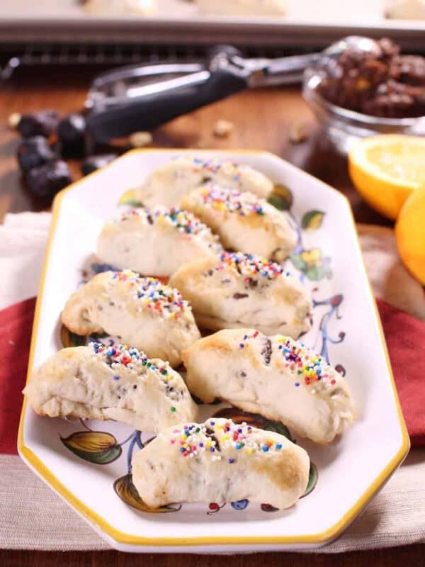 A plate of eight Cuccidati cookies topped with rainbow spinkles