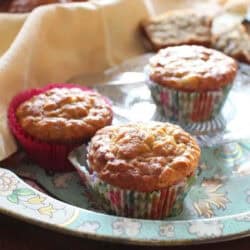 A tray of three Banana Oat Pecan Muffins with a basket of muffins in the background