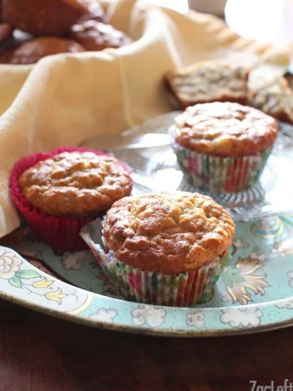 A tray of three Banana Oat Pecan Muffins with a basket of muffins in the background