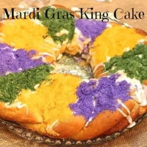 A whole king cake topped with white icing and purple, green, and yellow sanding sugar