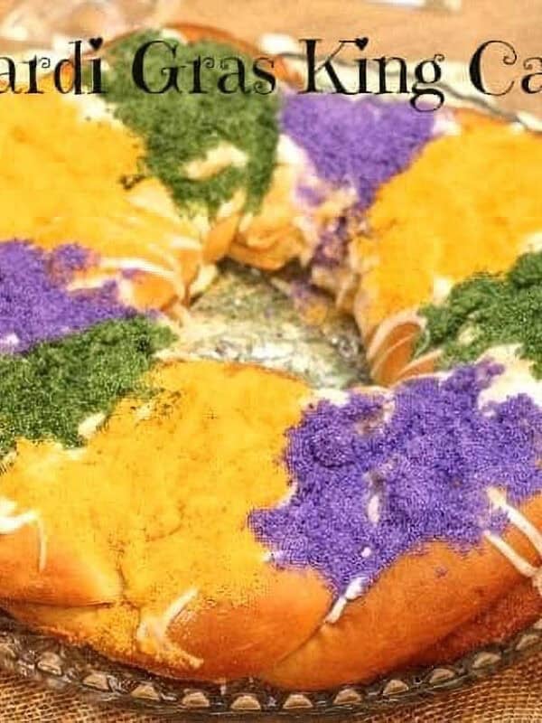 A whole king cake topped with white icing and purple, green, and yellow sanding sugar