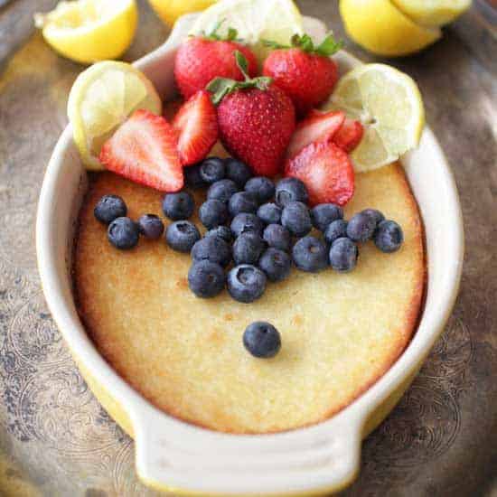 a cake baked in a yellow oval baking dish topped with blueberries, strawberries and slices of lemons.